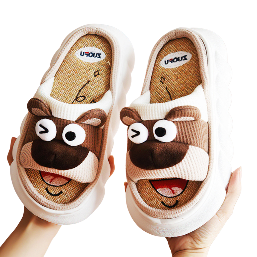 Pair of cartoon brown bear animal slippers held by a hand on a white background