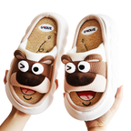 Pair of cartoon brown bear animal slippers held by a hand on a white background