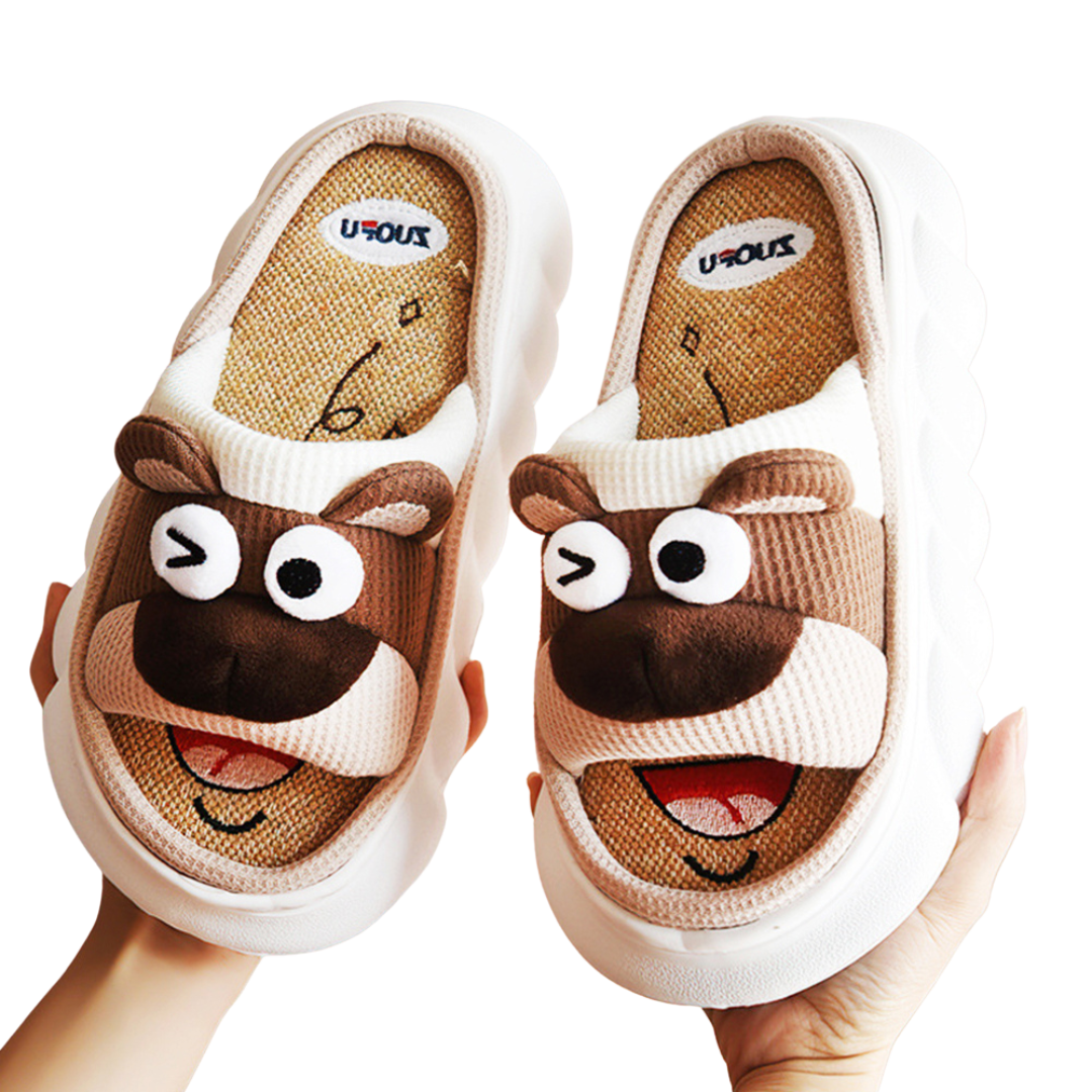 Pair of cartoon brown bear animal slippers held by a hand on a white background